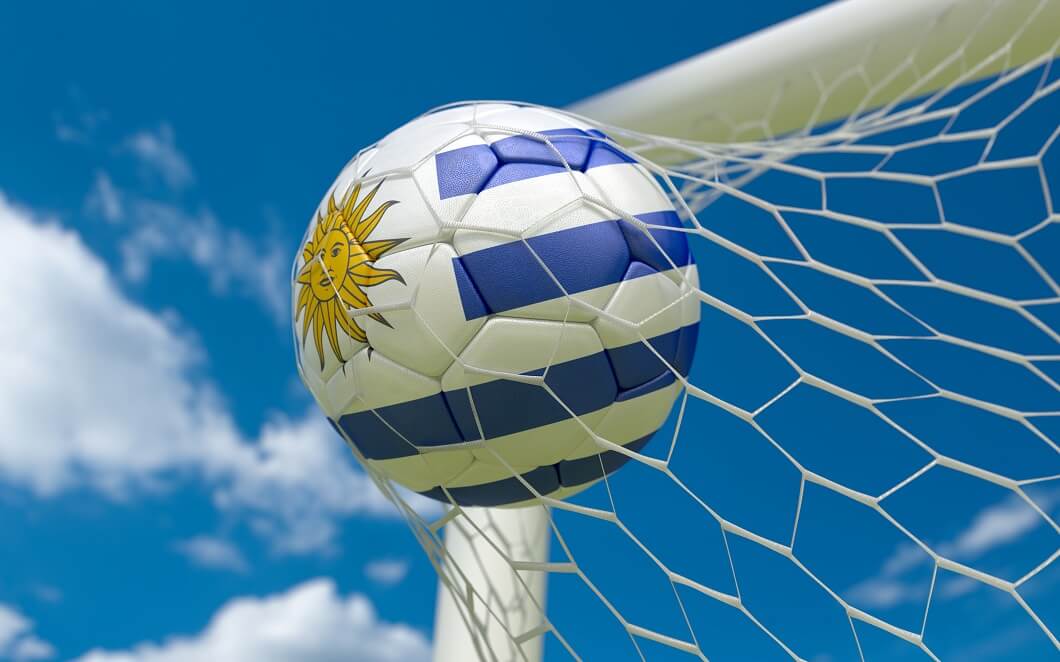 Bandera de Uruguay y balón de fútbol en la red de la portería.